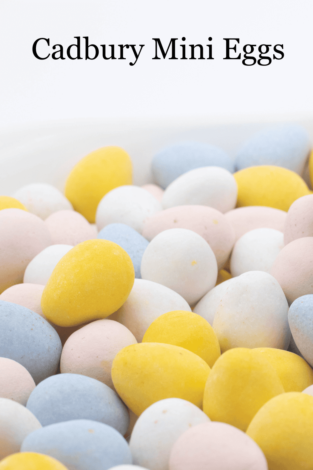 alot of Cadbury mini eggs on a white background, yellow, white, pink, white.