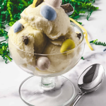 The Best Ninja Creami Vanilla Protein Ice Cream creamy ice cream in a parfait glass with a spoon cadbury mini eggs mixed in and green easter grass in the background.