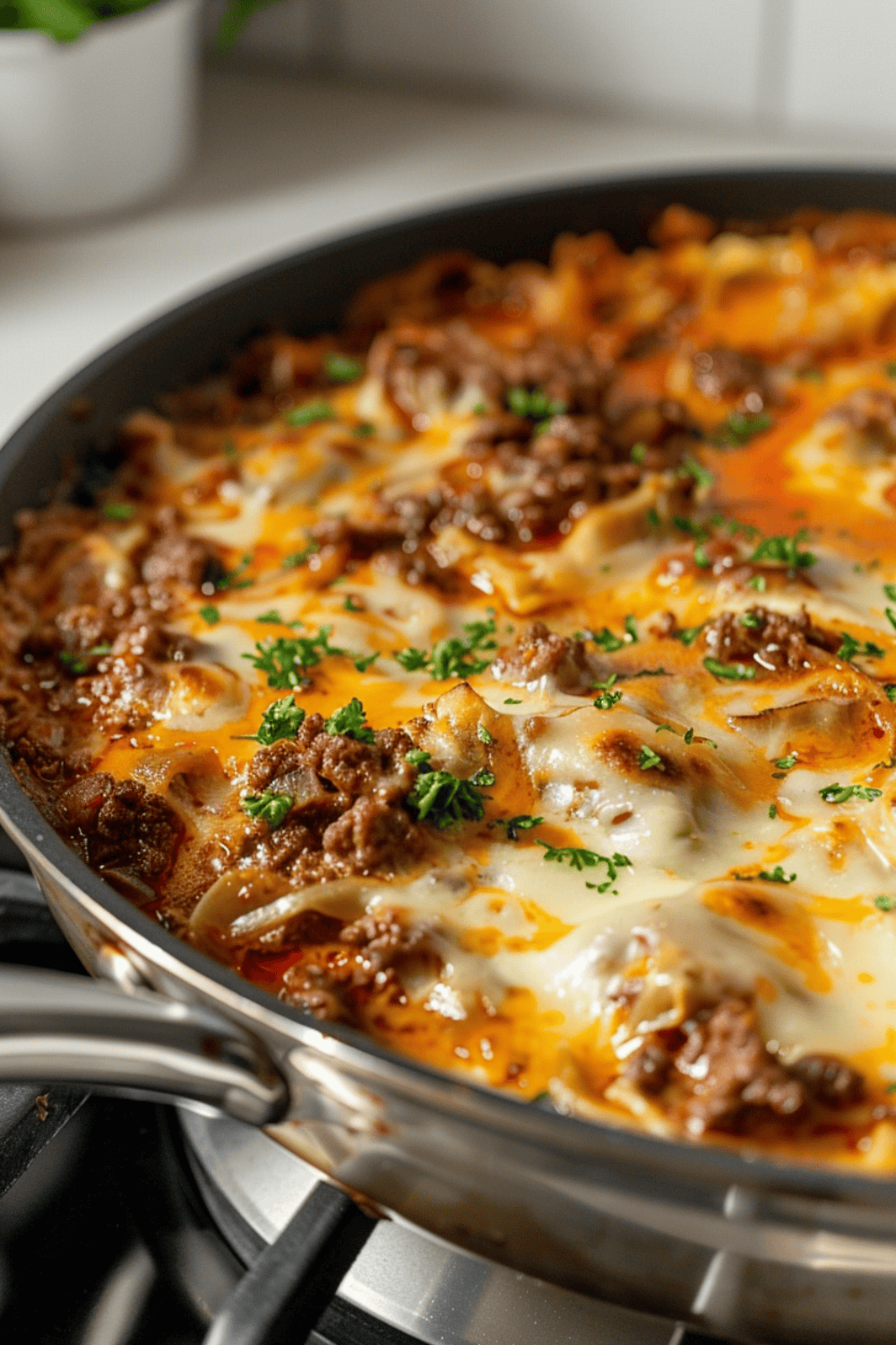 Unstuffed Ground Beef Cabbage Roll Casserole One-Pan in a pan on a gas stove with cheese and parsley on top in a white kitchen.
