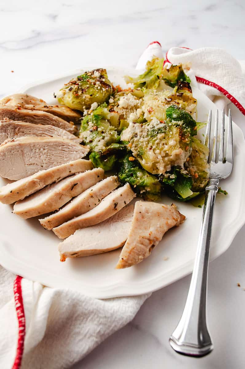 Tender Crispy Super Easy Air Fryer Chicken Breast sliced on a white plate with mashed brussel sprouts fork on the right and white towel with red trim.