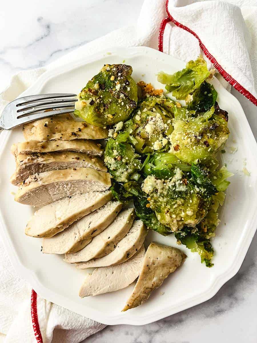 Tender Crispy Super Easy Air Fryer Chicken Breast sliced on a white plate with mashed brussel sprouts fork on the left top top down view.