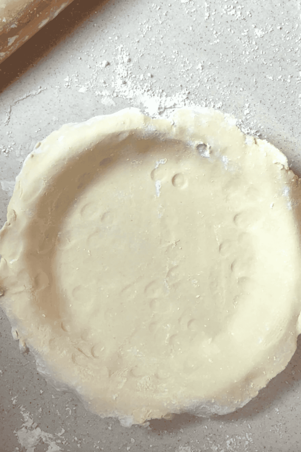 Uncooked pie crust laid in a pie pan on the kitchen counter with a rolling pin top left.