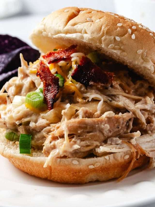 Slow Cooker Cream Cheese Crack Chicken Bacon and Ranch. on a bun with sesame seeds on top and blue corn chips on the plate.