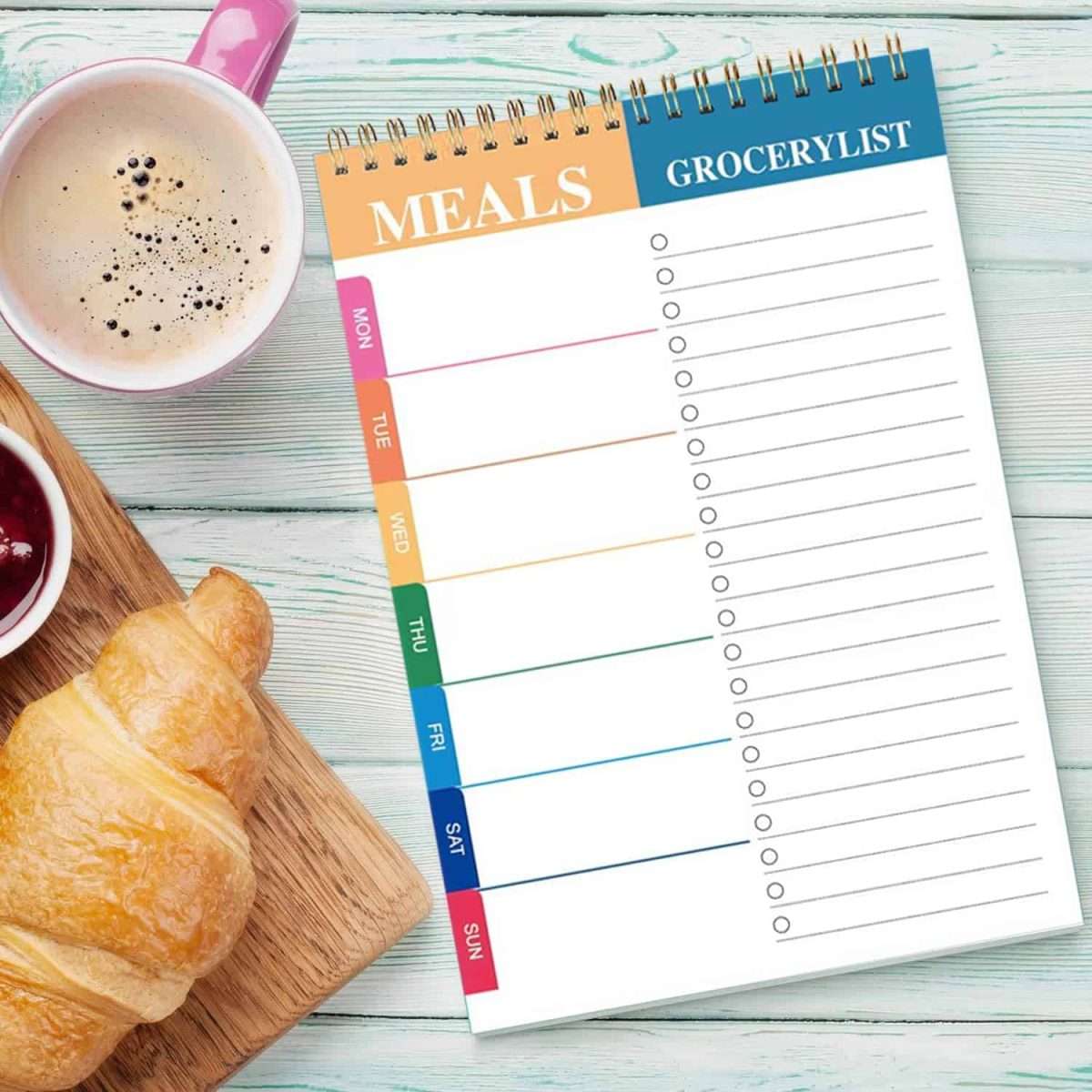 A top spiral pad that is for meal planning with a cup of coffee and croissant on the team.