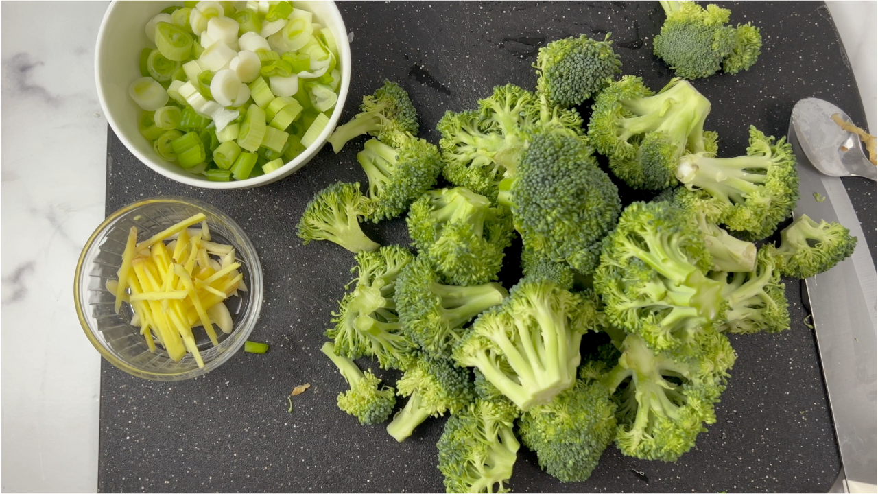 chopped broccoli, green onions and ginger on a black cutting board