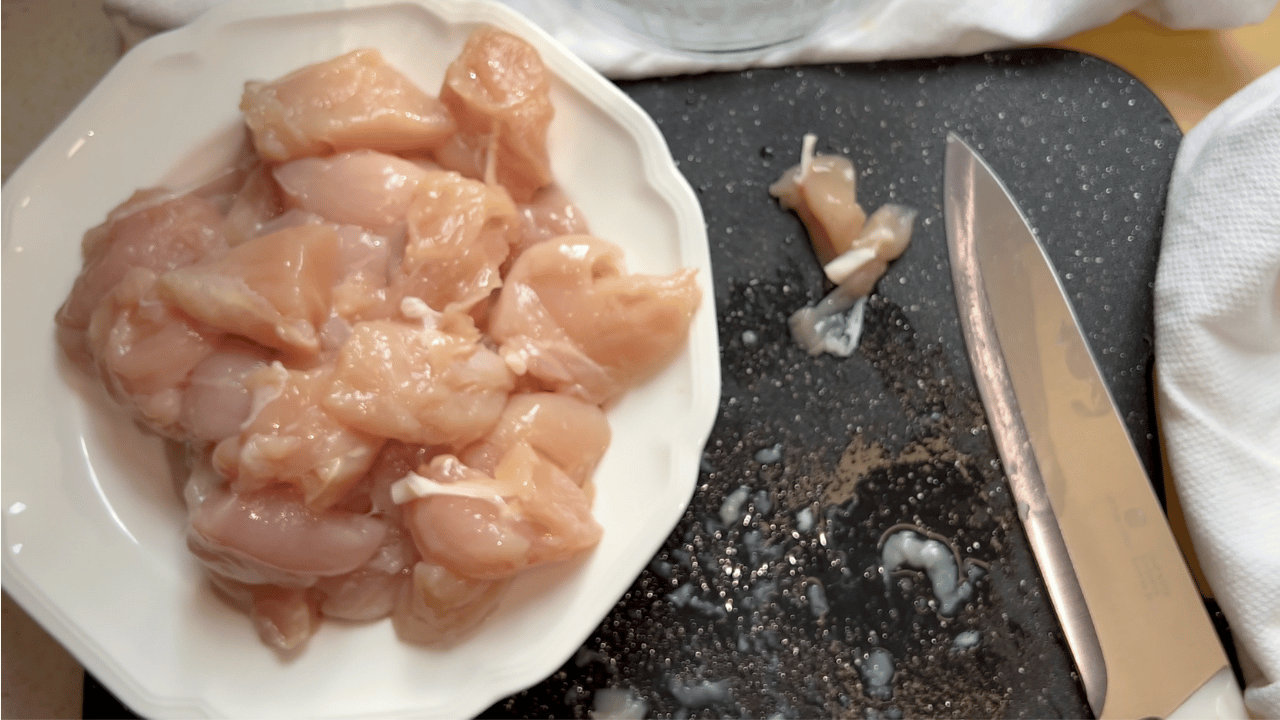 bite-size chicken cut up on a white plate on a black cutting board with a knife and white towel.