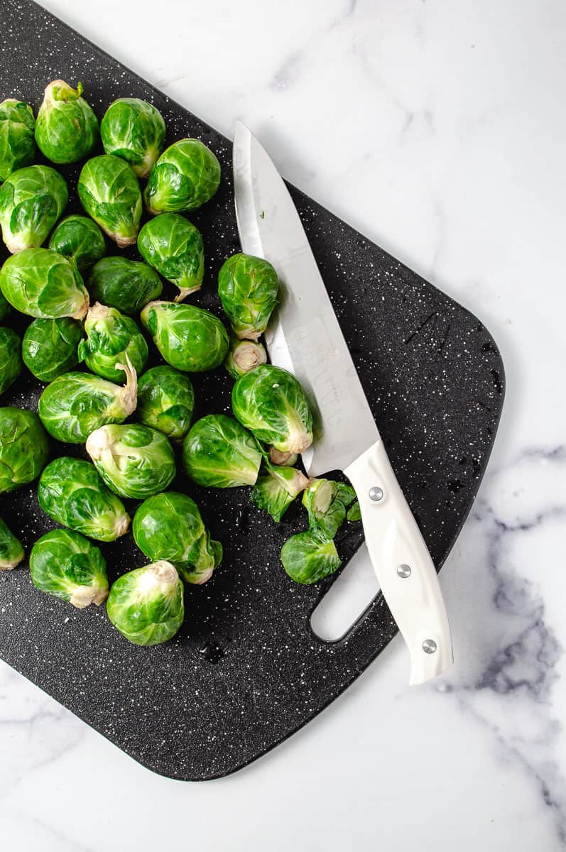 Easy Crispy Parmesan Smashed Brussels Sprouts on a black cutting board with a white knife trmining the ends.