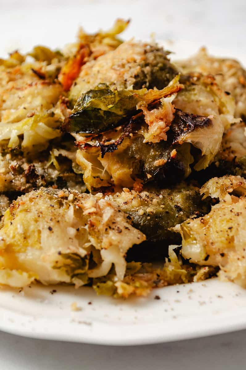 Easy Crispy Parmesan Smashed Brussels Sprouts close up of the golden brown delicious crispy sprouts on white plate.