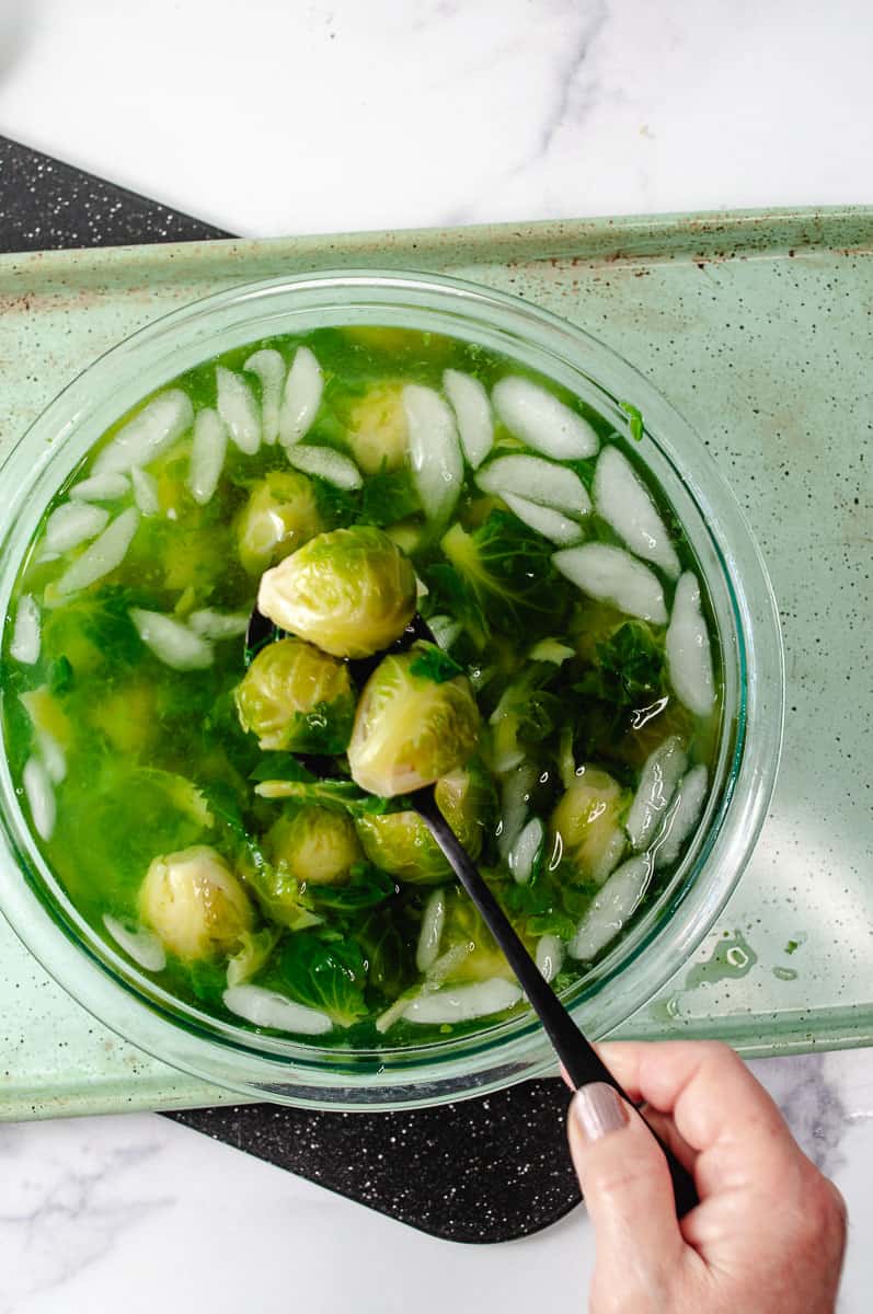 Easy Crispy Parmesan Smashed Brussels Sprouts removing from a ice water bath on a green pan on a white counter.