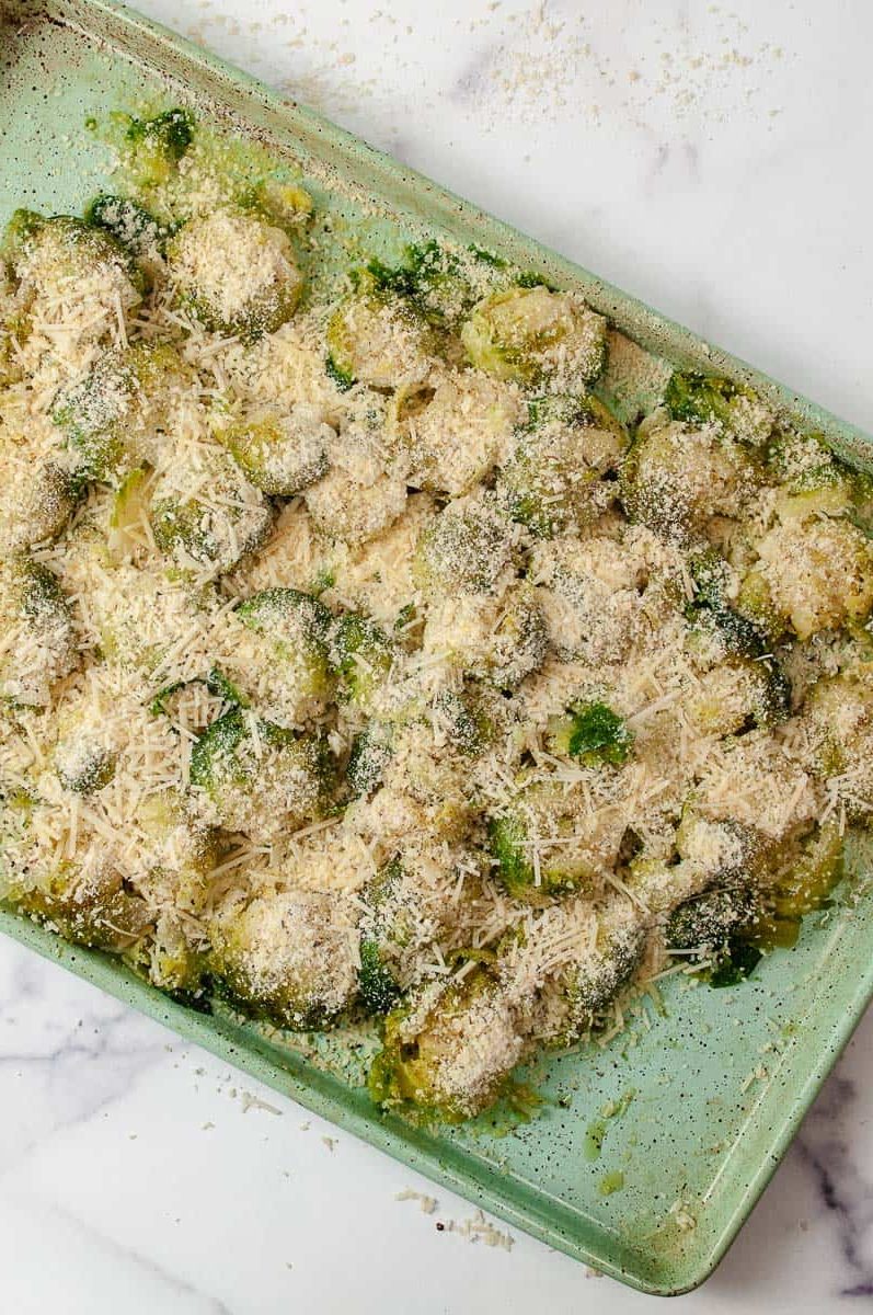 Easy Crispy Parmesan Smashed Brussels Sprouts smashed sprouts on a green baking pan with cheese and spices prior to baking