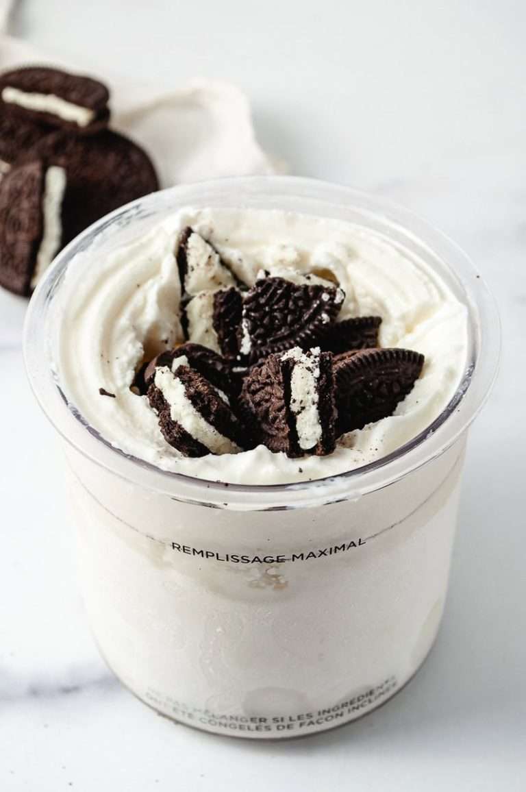 ninja creami cookies and cream pint jar with vanilla base ice cream and oreo cookie pieces on top and oreo cookies in the background.