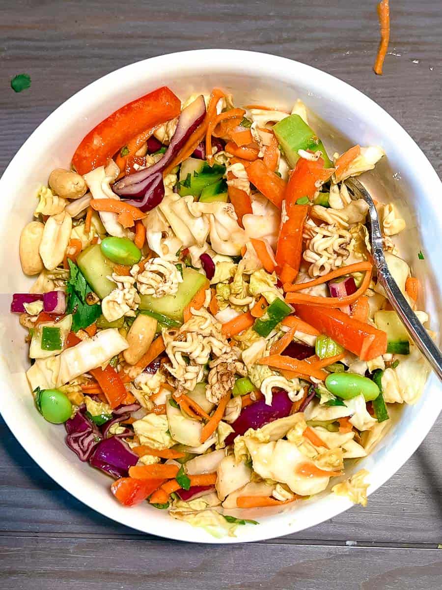 thai crunch salad close up of all the veggies with peanuts and ramen noodles on top in a white serving bowl with a fork.