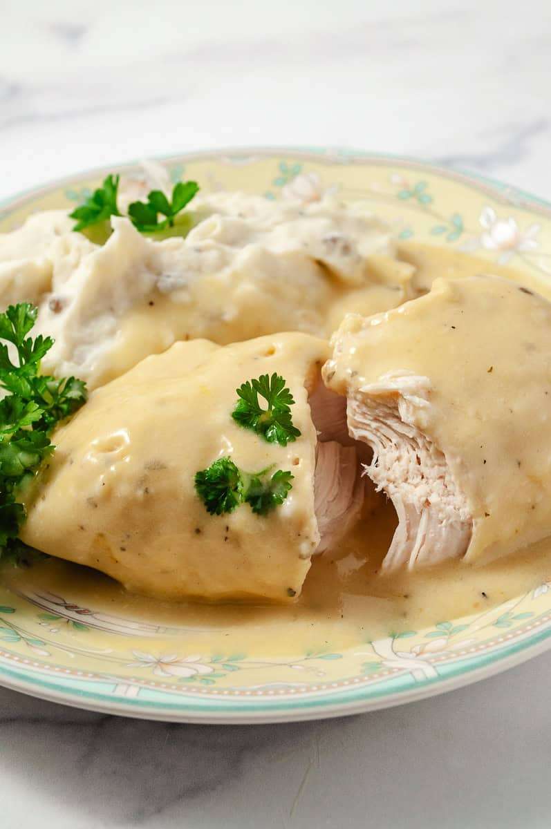 creamy crockpot dry ranch dressing chicken breast cut open on a green and yellow flowered rimmed plate with mashed potatoes and parsley.