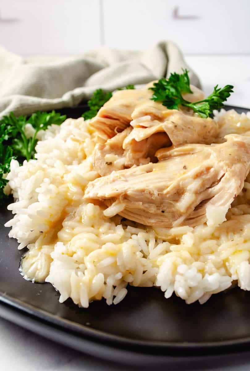 Creamy CrockPot Dry Ranch Dressing Chicken 5-Ingredients on a bed of rice on a black late with parsley spring on top of the chicken and the side of the dish with a fork and a green napkin top left.