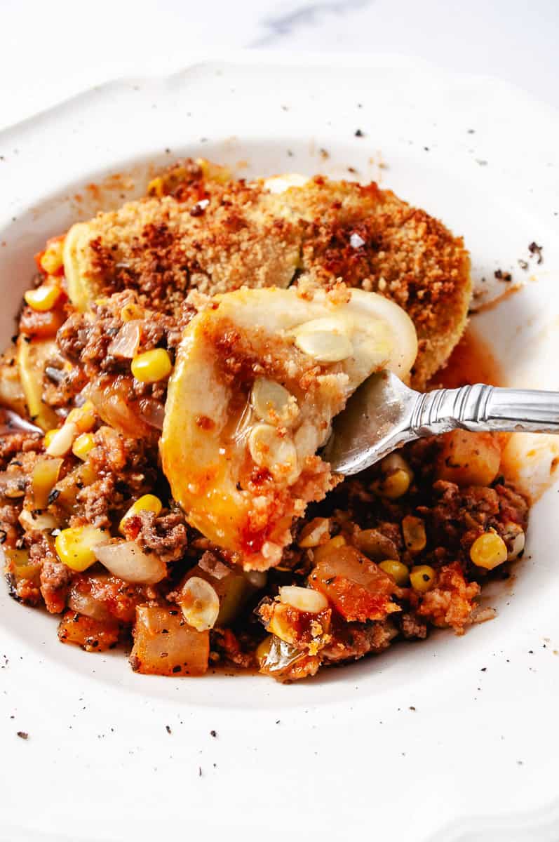 Easy Ground Beef Zucchini Skillet Casserole Low Carb in a white bowl and a fork with a zucchini slice on a fork, onion, corn, zucchini and beef visible