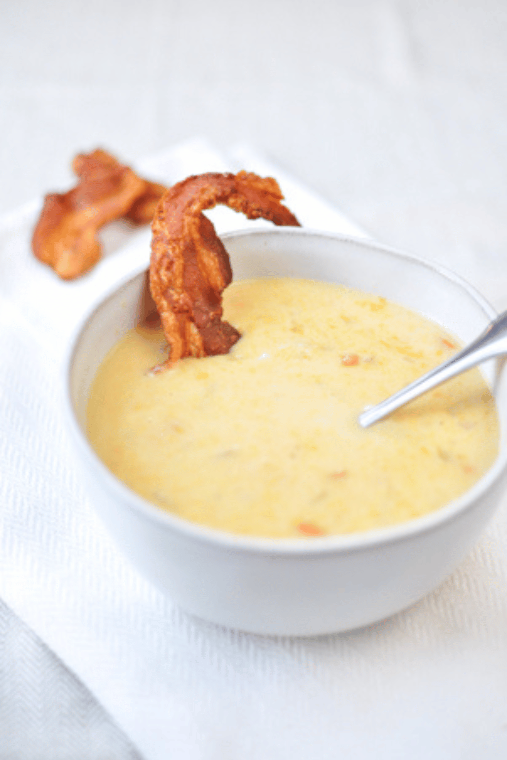 beer cheese soup with bacon in a white bowl on a white counter.
