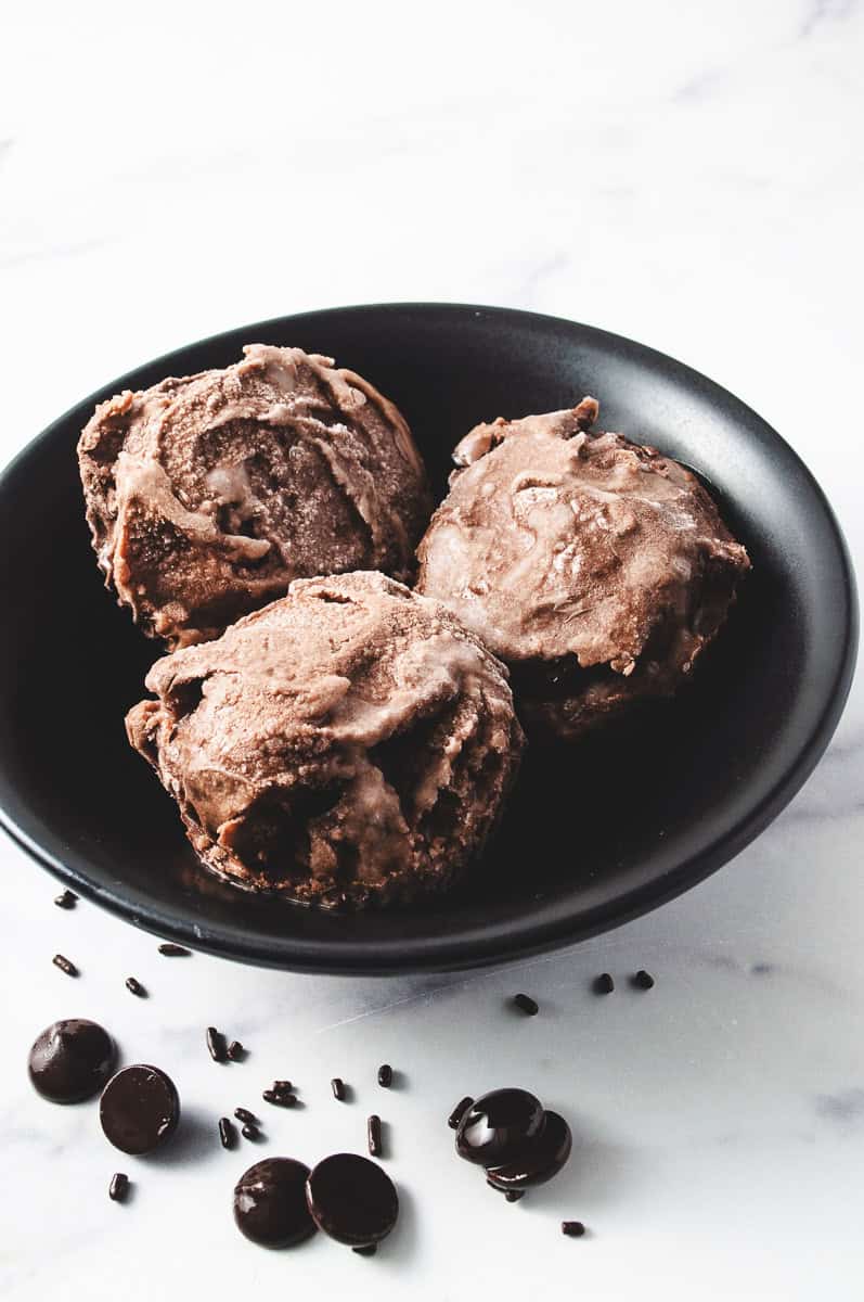 Ninja Creami Chocolate Ice Cream-Special Dark Cocoa 3 scoops in a black round bowl on a white counter with chocolate sprinkles and chocolate chips on the counter.