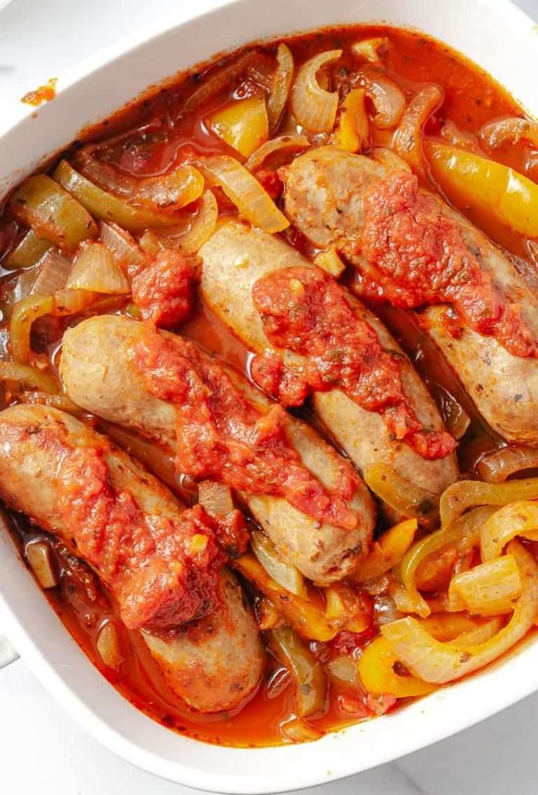 close up of the Easy CrockPot Italian Sausages Peppers Onions a white square serving dish with 4 sausages with the onion, pepper and tomato sauce top down view.
