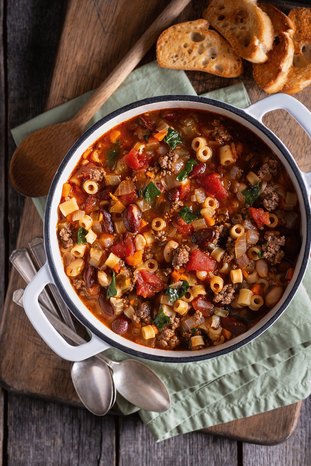 pasta fagioli soup in a dutch oven with a wooden spoon top down view.