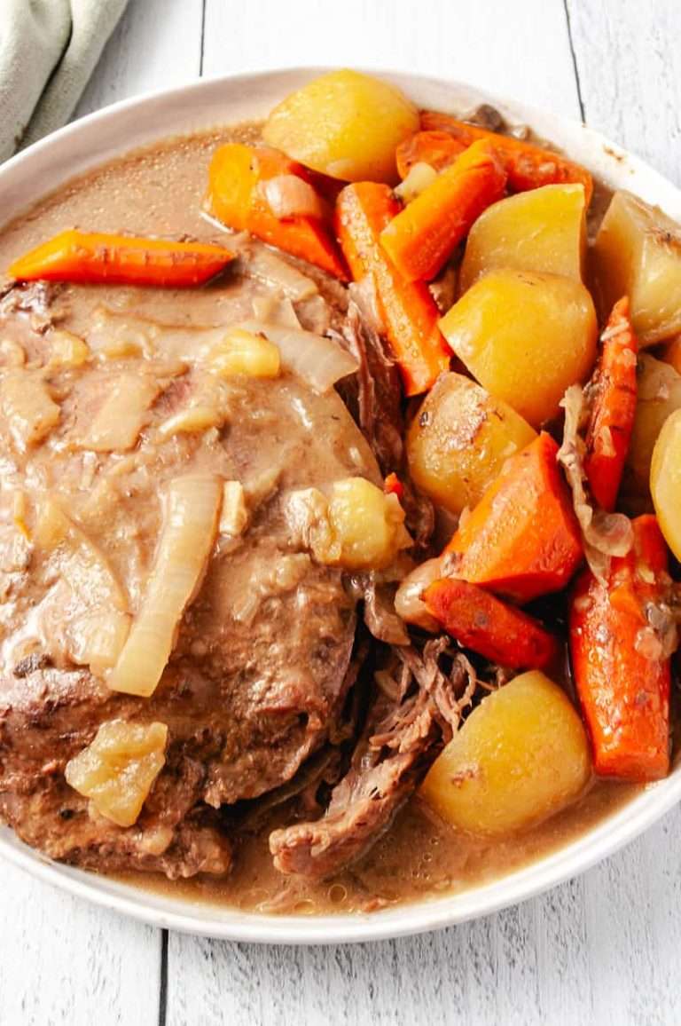 Easy Slow Cooker Pot Roast Lipton Onion Soup Mix on a round white plate with onions, carrots and potatoes on a white wood table close up of the roast.