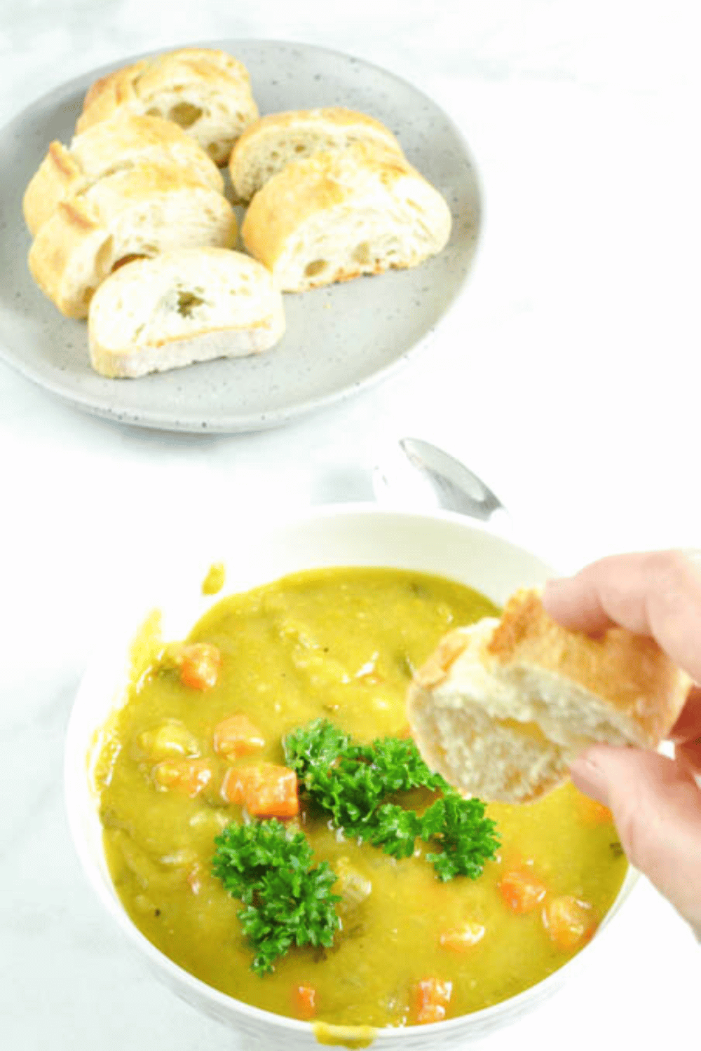 Simple Instant Pot Split Pea Soup with Ham on a white table, with a late of bread and a hand dipping bread into the soup.