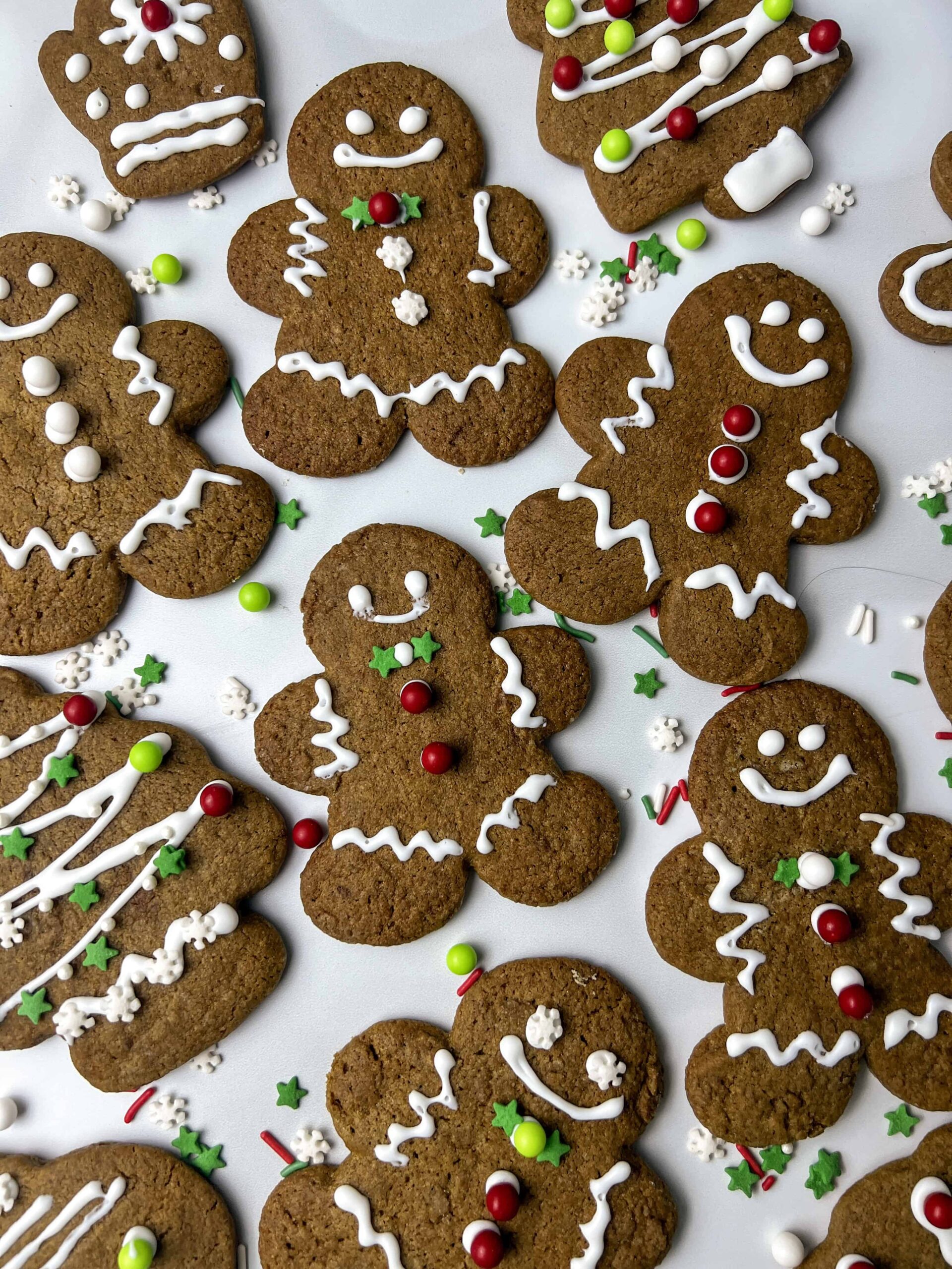 gingerbread men on a white counter with white frosting and decoration with sprinkles.