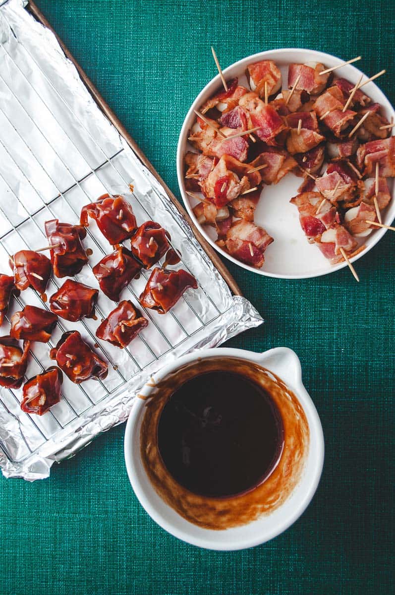 Bacon Wrapped Water Chestnuts with Pre-Cooked Bacon (Rumaki) a over head view of the bacon wrapped water chestnuts on a white plate and some dipped in the sauce and the sauce in a small white bowl. 