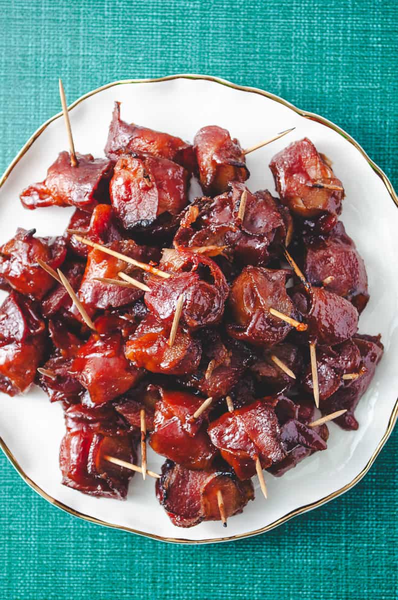 Bacon Wrapped Water Chestnuts with Pre-Cooked Bacon (Rumaki) top down view of the cooked water chestnuts on a white ruffle plate with a gold edge.