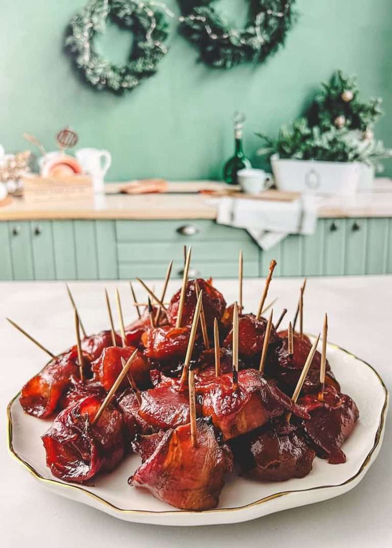 bacon wrapped water chestnuts on a white ruffled plate on a white counter and a christmas green background