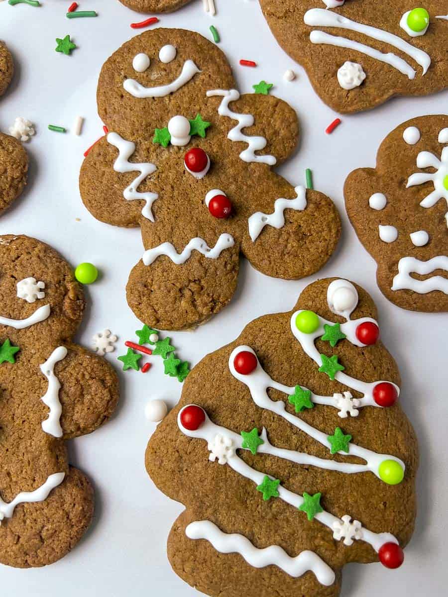Soft gingerbread men cookies decorated with white icing, red and green candy buttons, star sprinkles, and festive details on a white background, perfect for Christmas cookie decorating.