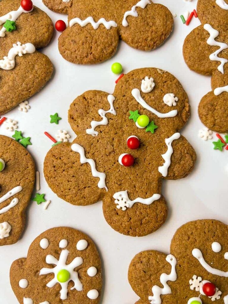 Soft gingerbread men cookies decorated with white icing, red and green candy buttons, and festive sprinkles on a white surface, perfect for Christmas baking and holiday cookies.