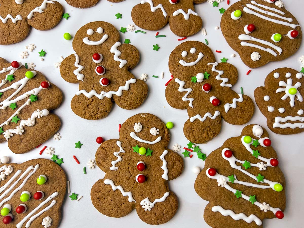 Soft gingerbread men cutout cookies with smiling faces, wavy white icing details, and red and green candy buttons scattered on a white surface, perfect for Christmas cookies and holiday baking.