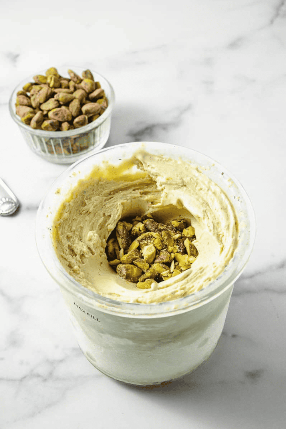 Pistachio Ice Cream Ninja Creami in the ninja creami pint with nuts in the center to be mixed in and a small bowl with pistachio nuts.