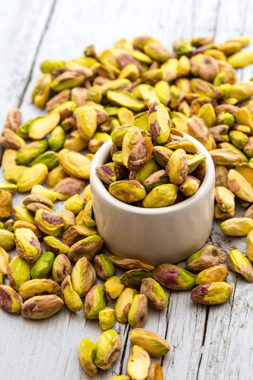 Pistachio Ice Cream Ninja Creami nuts in a small round bowl and al ot on a wood table