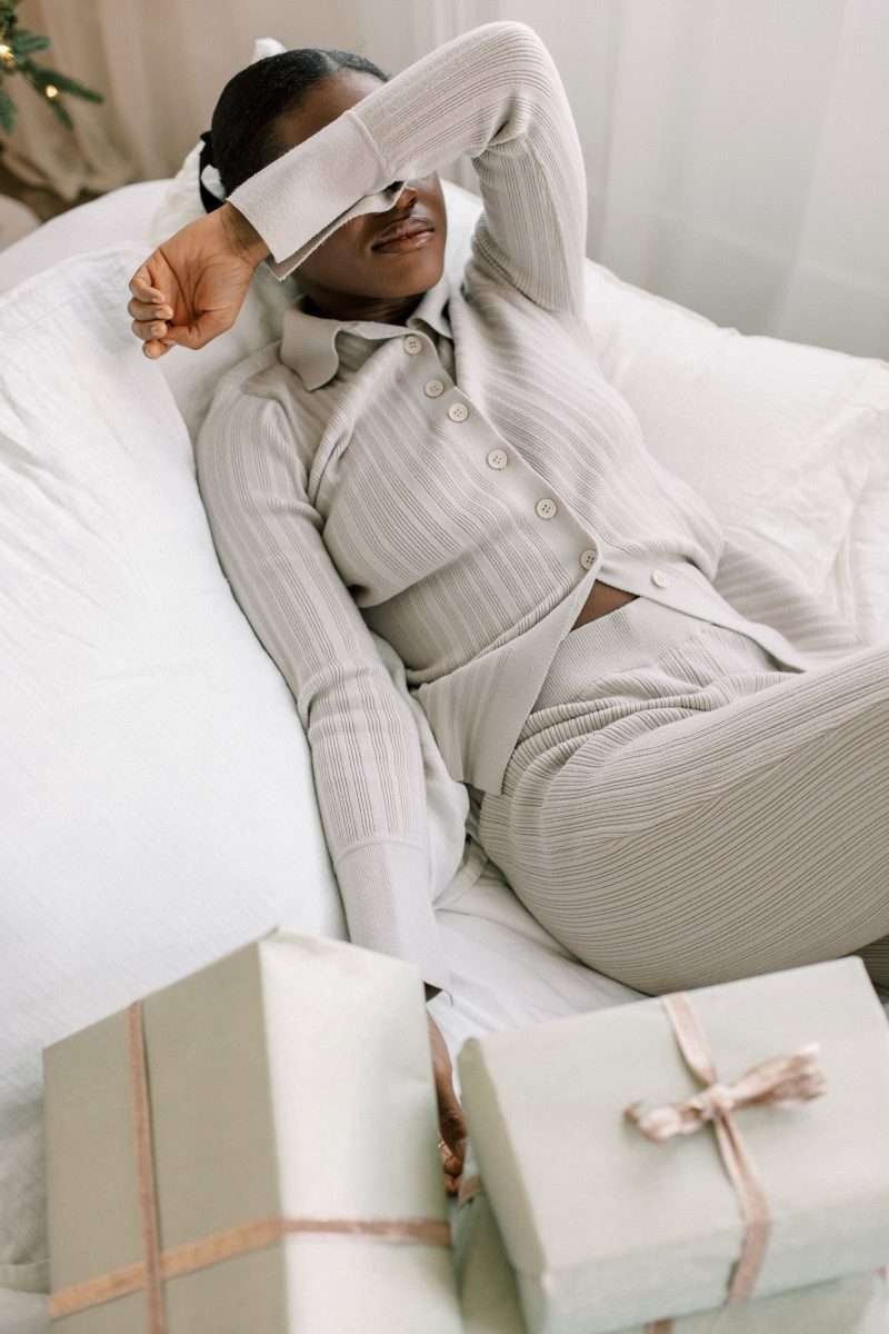 Using the Envelope System: A Beginner’s Budgeting Guide Woman laying on a bed with a lot of packages with her hand over her head overwhelmed.