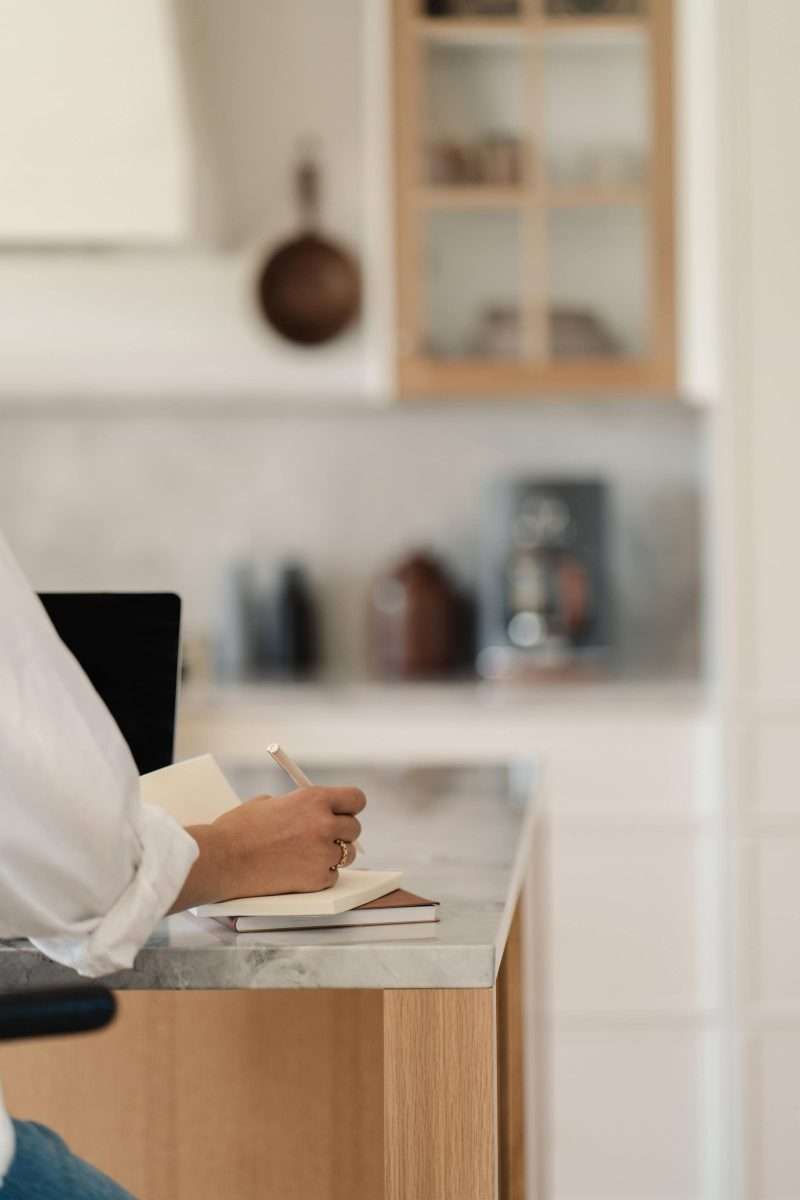 budgeting envelope system woman's aren writing a budget worksheet on a kitchen counter.