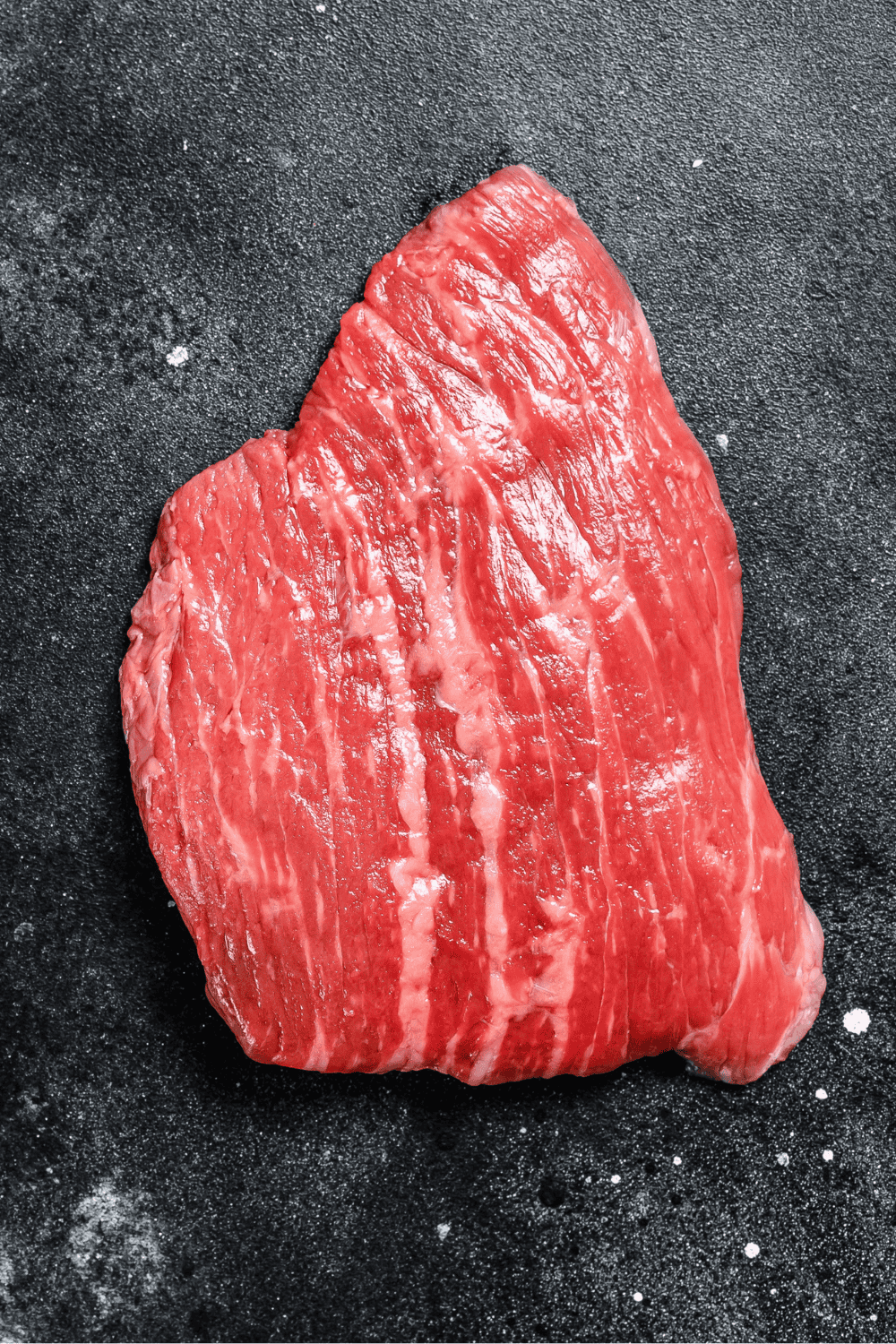 uncooked flank steak on a black cutting board