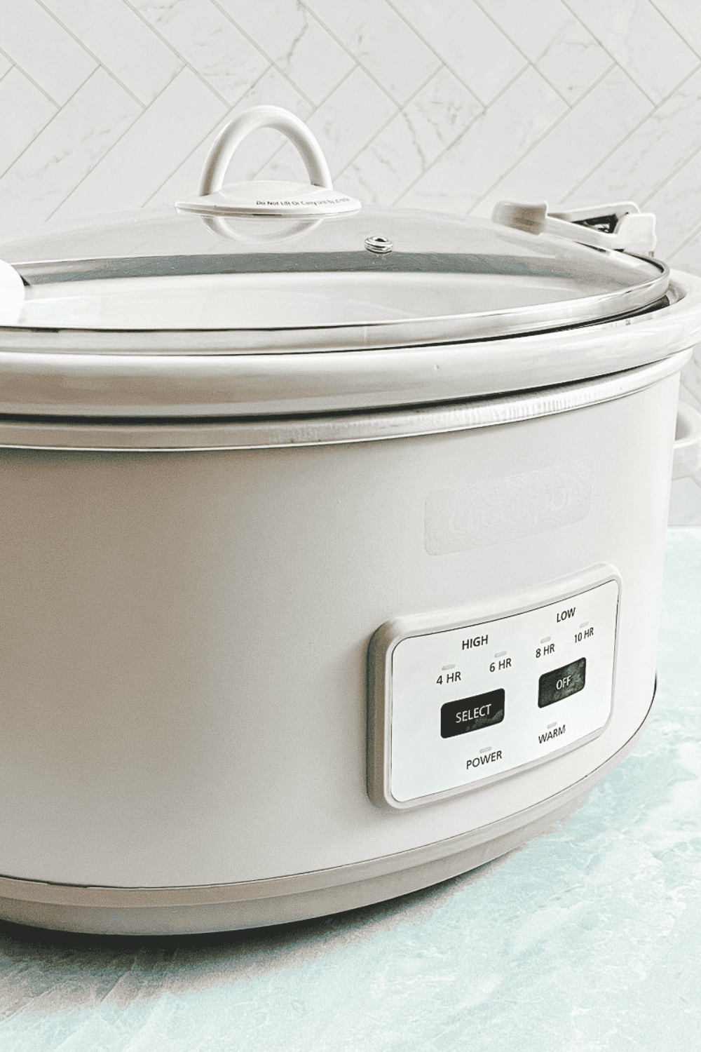 cream crockpot with lid on a green counter side view