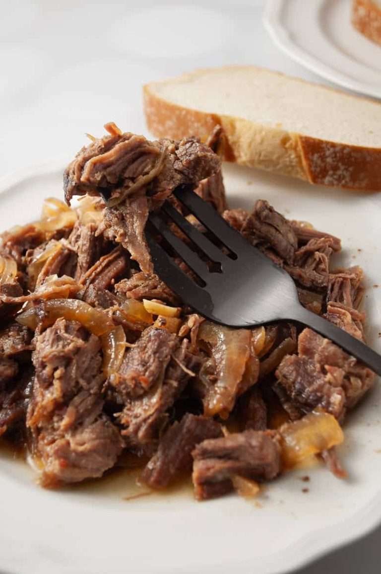 teriyaki flank steak slow cooker white plate with a pile of shredded flank steak with bits of onion on a black serving fork with a slice of bread crockpot recipe