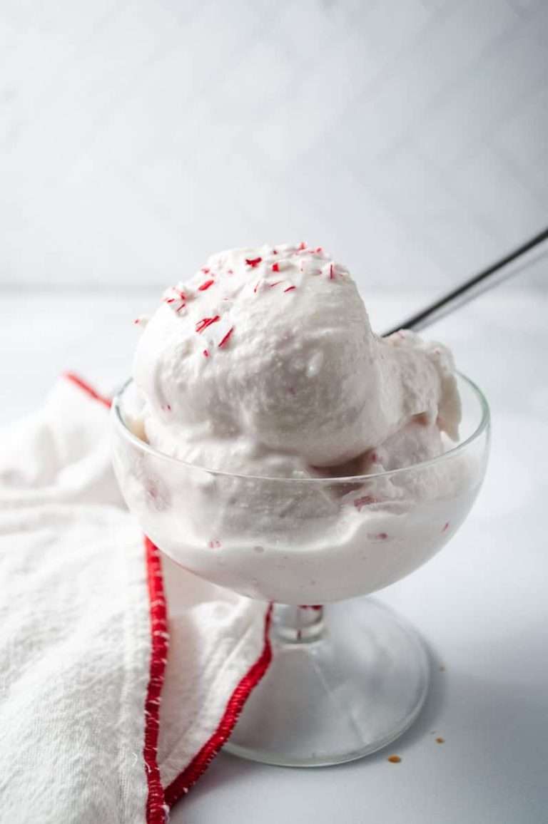 Ninja Creami Peppermint Ice Cream Holiday Treat 2 scoops in a clear parfait cup with a towel with a red trim and crushed peppermint candy cane on top with a spoon.