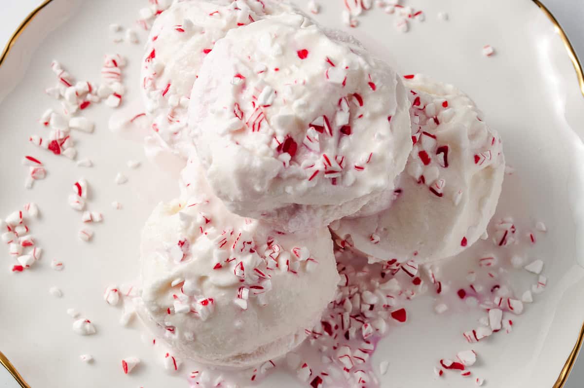 top down view of Ninja Creami Peppermint Ice Cream Holiday Treat 3 scoops on a white plate with a gold trim and crushed candy cane on top.  