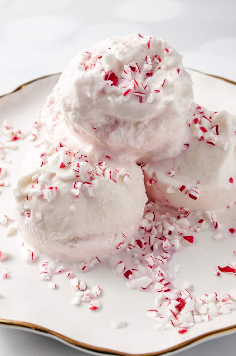 Ninja Creami Peppermint Ice Cream Holiday Treat 3 scoops on a white plate with a gold trim and crushed candy cane on top. 