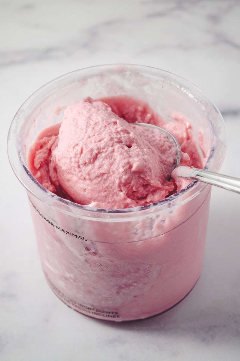 Ninja Ceami Protein Strawberry Ice Cream with Fairlife Milk, ninja creami pint with creamy ice cream bright pink with a spoon scooping out some ice cream. 