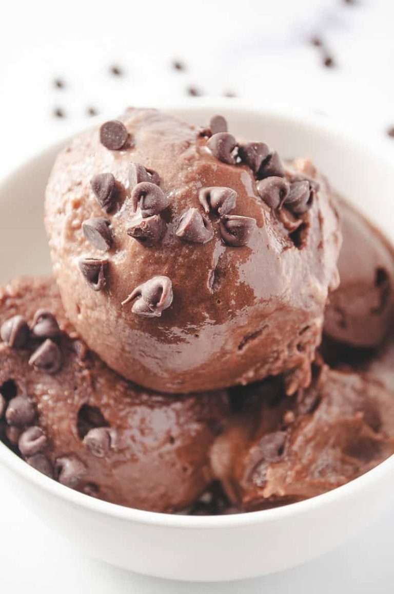 Ninja Creami Protein Chocolate Ice Cream 3 scoop of creamy of ice cream with mini chocolate chips on top, in a white bowl with chocolate chips scattered on the counter, Close up of the top of the ice cream.