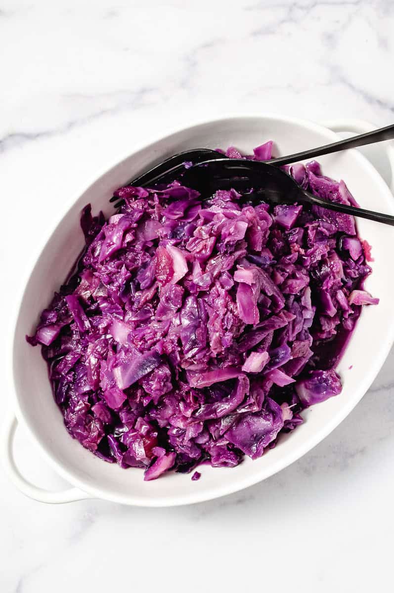 Instant Pot German Red Cabbage with Apple in a white serving bowl with serving utensils.