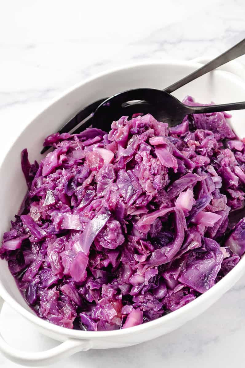 Instant Pot German Red Cabbage with Apple in a white serving bowl with serving utensils. 