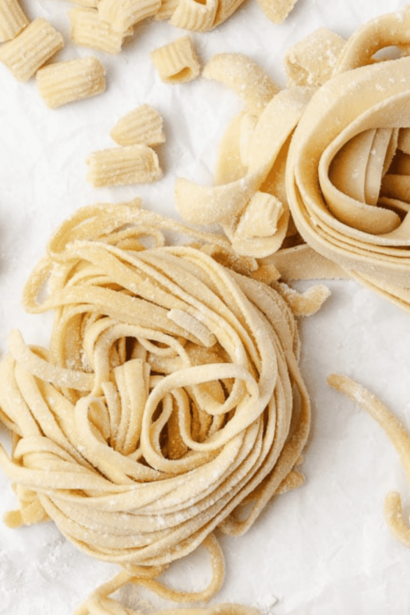 How to Make Homemade Fresh Pasta Using Pasta Maker fresh made 2swirls of pasta and mini elbow pasta on a parchment paper top view.