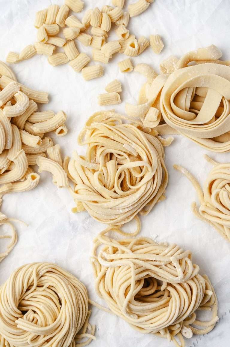 How to Make Homemade Fresh Pasta Using Pasta Maker fresh made 4 swirls of pasta and 2 elbow pasta on a parchment paper top view.