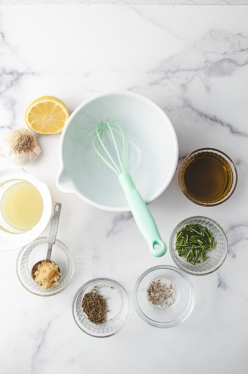 Ingredients for a Chicken Skewer Marinade including lemon, garlic, olive oil, rosemary, spices, and a whisk in a mixing bowl—perfect for quick weeknight meals and grilled chicken skewers. This setup is ideal for making easy chicken skewer marinade recipes to enhance kabobs on the grill.