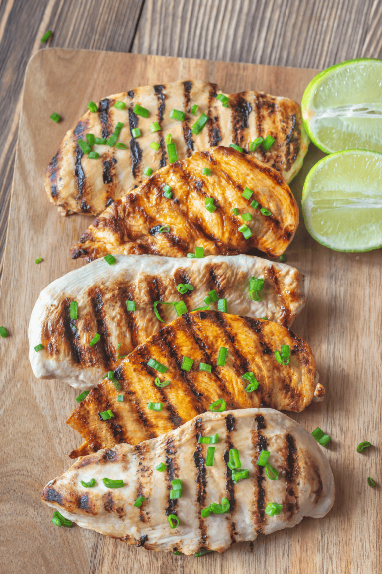 Grilled chicken breasts arranged on a wooden board, garnished with fresh green onions and lime halves, perfect for a coconut lime chicken dinner. This juicy and flavorful dish uses a coconut chicken marinade blended with citrusy lime sauce, inspired by a light and tropical Thai coconut lime chicken recipe.